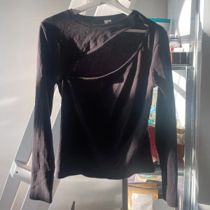 Svart ribbad topp med cut out från NLY Trend - Säljer en svart långärmad ribbad topp från NLY Trend med en snygg cut out-detalj över bröstet. Toppen har tight passform och rund halsringning. Perfekt för dig som vill ha något trendigt och stilrent!