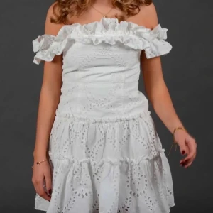 Zara vit klänning - Superfin vit kortklänning med offshoulder och volang upptill. Klänningen har broderade hålmönster och en luftig, somrig känsla. Perfekt för varma dagar och som studentklänning/avsultningsklänning