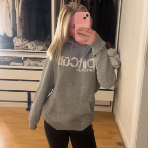 Grå hoodie  - Säljer en grå hoodie med vit logga på bröstet. Tröjan har huva med dragsko och en stor magficka. Perfekt för en avslappnad stil.