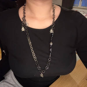 Två halsband med kedjor och detaljer - Säljer två halsband: ett i silverfärg med döskalleberlocker och svarta pärlor, samt ett i guld med glittrigt hjärthänge. Båda har grova kedjor och unika detaljer som sticker ut.