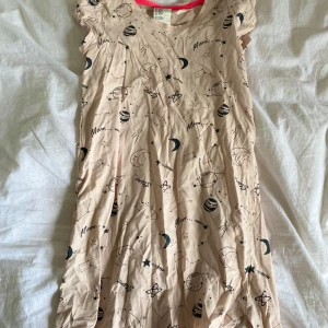 Beige klänning med rymdmönster från H&M - Säljer en beige klänning från H&M med coolt rymdmönster som planeter, stjärnor och månar. Klänningen har korta ärmar och rund halsringning med rosa kant. Perfekt för dig som gillar unika prints och bekväma plagg!