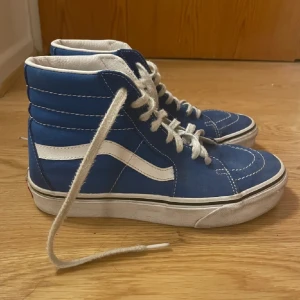 Blåa Vans Sk8-Hi sneakers - Säljer ett par klassiska Vans Sk8-Hi sneakers i blått med vit sula och vit sidosnirk. Höga skaft, vit snörning och tydliga kontrastsömmar. Perfekta för en streetwear-look och passar till det mesta. Fint skick sparsamt använda!