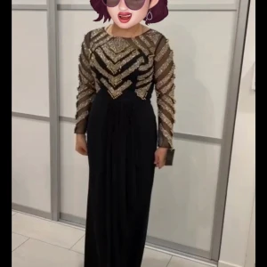 Svart långklänning med glittriga detaljer - Säljer en elegant svart långklänning med långa ärmar och glittriga mönster i guld på överdelen. Klänningen har rund halsringning och en figurnära passform upptill. Perfekt för festliga tillfällen! Helt nytt Använd ej, jag köpte på 2500kr 