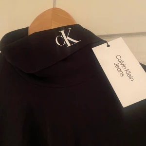 Svart polotröja från Calvin Klein Jeans - Säljer en svart långärmad polotröja från Calvin Klein Jeans med vit logotyp på ärmen och CK-märke vid kragen. Tröjan är i stretchigt material och har en tight passform. Perfekt att styla till olika outfits.
