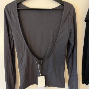 Mörkgrå långärmad topp med öppen rygg - Säljer en mörkgrå långärmad topp från Gina tricot med djup öppen rygg. Toppen är tight i modellen och har en stilren, minimalistisk look. Perfekt för dig som vill ha något enkelt men ändå med en twist. Kommer passa perfect i sommar. 💗💗