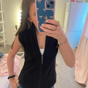 Svart fleeceväst från Everest - Svart väst i fleece från Everest med dragkedja framtill och hög krage. Perfekt att slänga över en tröja för extra värme. Enkel och stilren design utan ärmar.