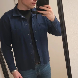 Mörkblå overshirt med knappar - Snygg mörkblå overshirt med klassisk krage och knäppning framtill. Skjortan har två bröstfickor och långa ärmar. Perfekt att bära över en t-shirt för en avslappnad stil.