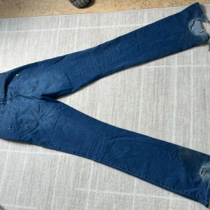 Blå bootcut jeans med slitningar - Säljer ett par blå bootcut jeans med slitningar vid benslut. De är gjorda för långa ben! 