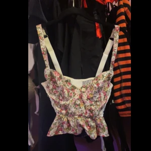 Blommig korsett-topp i fina vårfärger och vit broderad genomskinlig rygg 💕 - Blommig korsett topp med fina små blommor på!  Y2k / 2000s / 90s stil med volanger i botten av toppen.  Använt väldigt lite- för stor storlek :( Super snygg i nytt skick. Finns ej längre i lager eller butik på Urban outfitters! Eftertraktad och sällsynt 👀