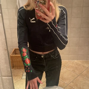 Croppad tröja 🌹 - Croppad, svart Pumatröja med vita ränder och rosor på ärmarna. Brett resårband i midjan. Storlek S men liten i storlek och långa ärmar. 100kr + frakt