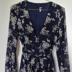 Blommig klänning (Dennis Maglic) - Säljer denna somriga blommiga klänning i färgen blå från Dennis Maglic. Det svalkande svävande tyget med bandet i midjan och den fina urringningen gör den lika söt som sexig. Den är ganska normal i storleken (S) men med bandet i midjan kan man välja längd