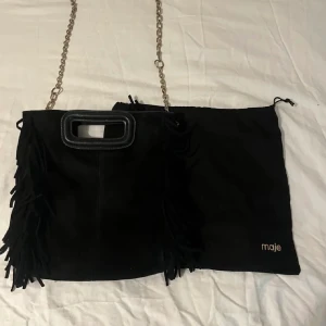 Maje väska - Svart väska ifrån märket Maje i den största storleken. Dustbag, svart band samt guldig kedja som är köpt separat från Maje medföljer. Väskan är använd en del men är i väldigt fint skick. Kan gå ner i pris vid en snabb affär!