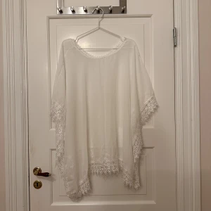 Strandponcho - Vit strandponcho, ONESIZE, tunt genomskinligt material med spets på kanterna runt om. Aldrig använd.