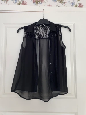 Blus - Svart genomskinlig blus med detaljer upptill i ryggen. Ingen ärm. Med knappar Egentlig storlek 150 men passar som en xs/s