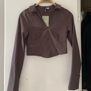 Brun tröja - Brun topp med slits i ärmarna. Aldrig använd men har sytt ihop urringningen en aning, prislapp kvar! Stl S