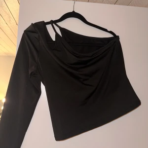 Topp från nelly - En svart topp från Nelly i storlek L med en arm som även har lite detaljer på ena axeln, i använd fåtal gånger🖤