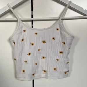 Blommigt linne/croptop - Säljer världens sötaste linne/croptop från Pull&Bear! Det är ett ribbat linne som på framsidan har små broderade solrosor och på baksidan är helt vit🌻 Svarar på frågor så fort jag kan! Om du vill köpa kan du trycka på Köp Nu💓💓