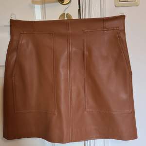 Ljusbrun kort kjol i skinnimitation. Dragkedja i sidan och 2 djupa fickor fram. Anv 2 ggr. Nu tyvärr för liten.