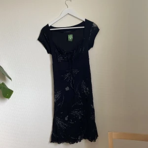 Svart klänning - En svart klänning från b.young. Klänningen har cap sleeves i mesh material, knytning fram i en slags milkmaid design och ett brett midjebälte som knyts i ryggen. Klänningen har ett mönster som är både i silver glitter och i velvet. 