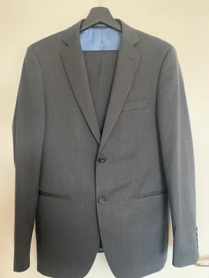 Dressman, kostym - Kavaj strl: 46  Byxor strl: 31-32 Gott skick, (dock är en av framknapparna på kostymen lite lös). Priset gäller hela kostymen.  