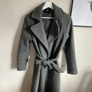 Lång kappa med skärp - Grå, lång, oversized kappa med skärp från bikbok! Lite nopprig men annars bra skick