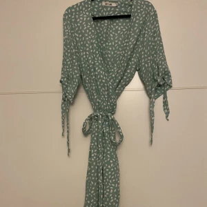 Omlott klänning i mint grönt med vitt mönster - Härlig sommar omlottklänning i mint grön med vitt mönster. Från Dry lake.  Använt två tillfällen förra sommaren. Passar tyvärr inte i storlek denna sommar.  Väldigt gott skick.  Nypris var 1,200kr Pris nu 500kr