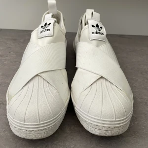Adidas skor - Ett par vita adidas sneakers, modellen liknar adidas super star fast med korsade band på framsidan, god kvalité. Jag är storlek 39 å skorna passar lätt någon som har storlek 40.