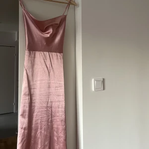 Klänning med fjädrar - Rosa festklänning i satin. Vadlång med rosa fjädrar längst ner. Fjädrarna är något slitna. Resår där bak och öppen rygg! 🩷 använd en gång! 