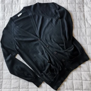 Kofta Merino Filippa K - Modell: "Merino Long Cardi" från Filippa K. Längre modell, finstickad. Fin kvalitet, 100% extra fin Merinoull. Handtvätt. Trasig på insidan: en infästning till fickan har lossnat - enkelt att laga själv. Fint skick i övrigt. Längd: ca 68 cm.