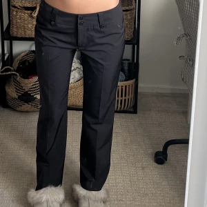 Bruna kostymbyxor  - Lågmidjade lite kortare i benen. Materialet är lite som en vindjacka, så lite hårdare och ”plastigare”.