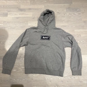 HOV1 merch - Grå HOV1 hoodie med tryck. Storlek S. Tröjan är ganska använd och tvättad, men inget som märks utvändigt. Säljer då den är för liten. 