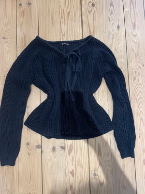 Stickad tröja med knytning - En blå stickad tröja med korsett format fram som gör att man kan välja hur stor urringning man vill ha eller om man inte vill ha nån