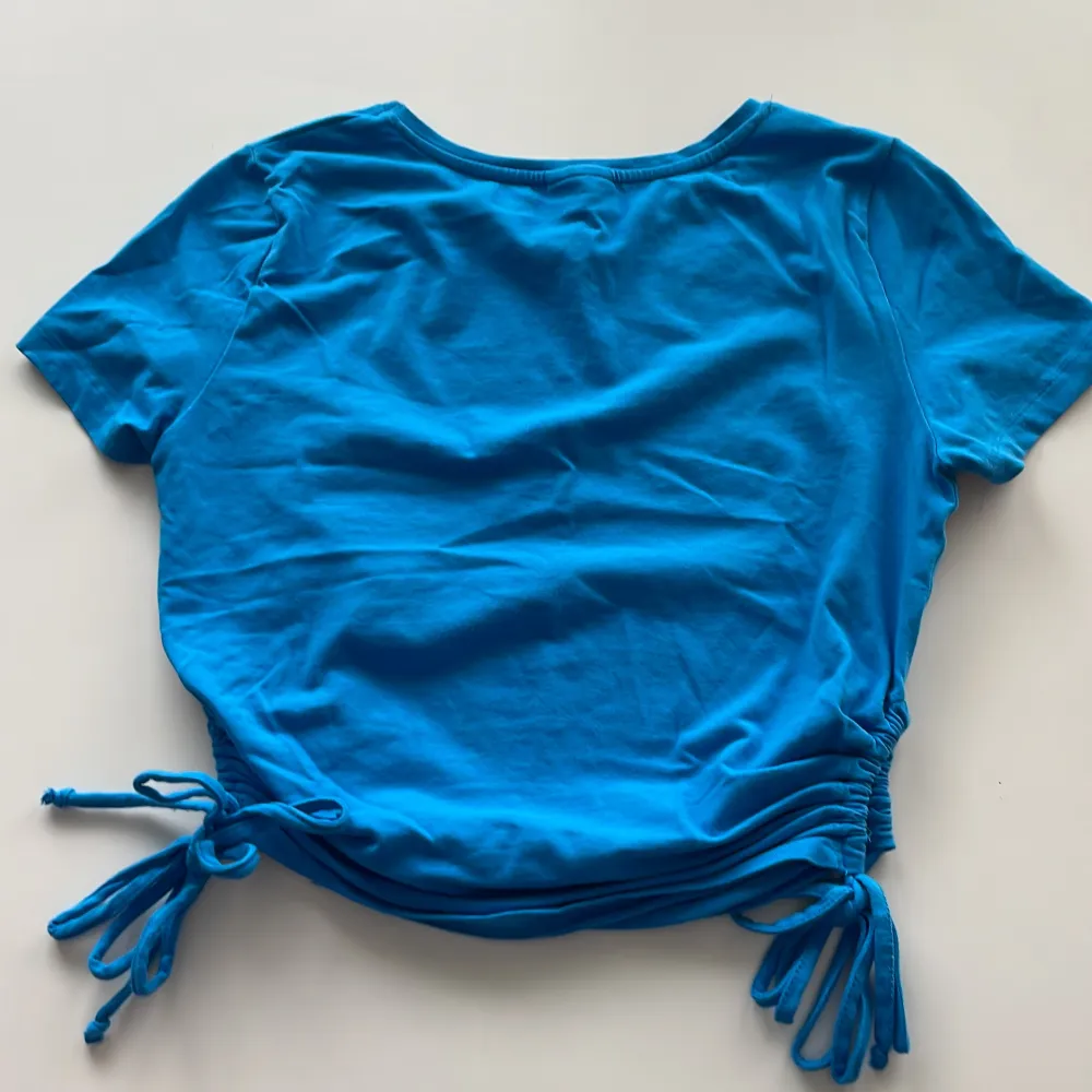 Jättesöt, blå tröja med snören som man kan knyta på sidan . T-shirts.