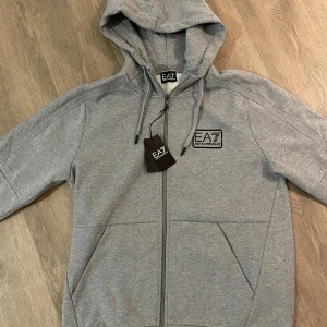 Emporio Armani EA7 Zip Hoodie storlek XL - Nya och oanvända med etikett. Finns i L och XL. Finns att hämta i Täby men kan även skickas mot fraktkostnad.