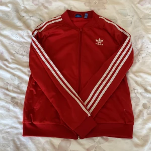 Röd adidas tröja med dragkedja. - Detta är en en thrifted adidas tröja med dragkedja. Den är väldigt bekväm men inte exakt min stil och är varför jag säljer den!   Det står även att det är storlek L eller M men egentligen så satt den ganska tajt på mig och jag har storlek S-M.
