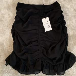 Säljer denna svarta draperade mini kjol från nakd då den ej kommit till användning. Den är i fint skick med lappar kvar. 