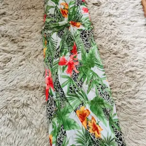 En färgstau festklänning med stora underbar🌺 blommor 🌺 och 🌿blad. One Size passar S-M  (har smören runt midjan)  