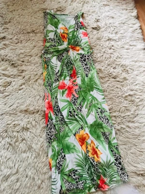 Färgglad festklänning  - En färgstau festklänning med stora underbar🌺 blommor 🌺 och 🌿blad. One Size passar S-M  (har smören runt midjan)  