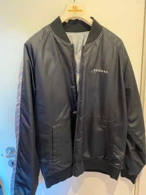 Nike Swoosh jacka - Helt ny Nike swoosh jacka den är i storlek M men passar L också. jackan är helt ny har använt den kanske 2 gånger. Man kan ta på sig jackan på både sidorna den ena sidan är svart och den andra grå. OBS: Köparen står för frakten.