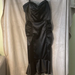 Aftonklänning Stop staring - Fin, glansig aftonklänning i retrostil från märket Stop staring. Vadlång, smickrande sjöjungfruform. Axelband, dragkedja bak. 90 % poly 10 % lycra strl XL (byst 101 cm., midja 76, höft 109) Kemtvätt. Använd en gång. 