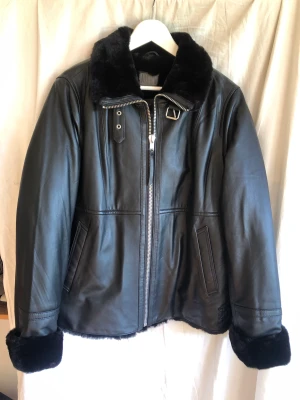Jofama Alice leather bomber - Fodrad läderjacka. Svenska kvalitets märket Jofama, Alice leather bomber i mjuk lammnappa med krage och insida av fejkpäls. Nypris 3300kr, aldrig använd. Rak modell, 2 fickor och 1 innerficka. Dragkedja går hela vägen upp i halsen. Ca 62 cm lång i stl 44