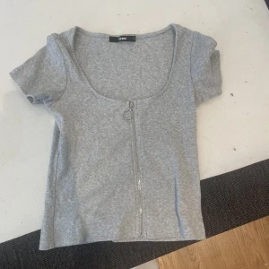 T-shirt med dragkedja - En grå T-shirt med dragkedja fram, från Bikbok i storlek XS.  Minns inte sist det användes men den är bara använd några få gånger för möjligtvis 1-2 år sedan annars har den bara legat i lådan.  Kan tvättas innan den skickas/hämtas 
