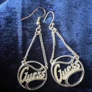 Guess örhängen  - Guess örhängen till salu, i äkta silver.  Som ni kan se så har jag tyvärr bytt ut den riktiga hängaren på ena (som fäst i örat) mot en icke silver då den riktiga kom till skada. Annars i väldigt fin skick.  Ord pris: 70 euro