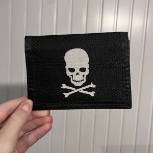 plånbok med dödskalle - en cool plånbok med en dödskalle på! ☠️den stängs med resårband och har har plats för minst 3 kort, två mindre fickor, en större ficka för sedlar och kvitton, och en ficka med dragkedja för mynt. insidan är gjort av plast och utsidan av tyg!