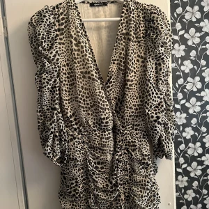 Kort klänning - Kort klänning från GinaTricot i leoparprint. Snören som man kan dra åt för ”scrunch”-effekt så att den blir kortare eller längre. Går till mitten av låren. Dragkedja på sidan. Storlek 38.