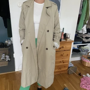 Trenchcoat  - Trendig trenchcoat med mörka knappar, i fint skick! 🥰 Finns band man kan knyta i midjan också. Ärmarna är uppvikta lite på bilderna men går att vika ner så man inte ser det randiga innertyget! 