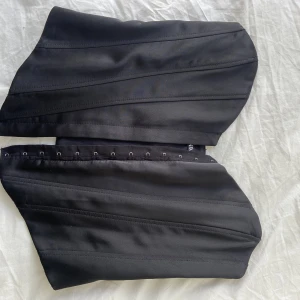 Svart korsett  - Supersnygg svart korsett i glatt tyg. Ganska liten i storleken. Detta är en S. Är du en 34 eller 36a skulle denna passa perfekt på dig. Jag själv är en bredaxlad 36a och den är lite, lite liten på mig. Jag har aldrig använt den, därav är prislappen kvar! 