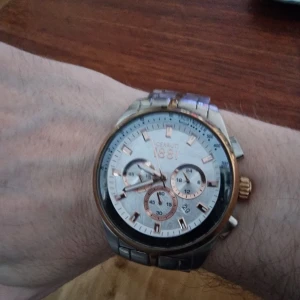 Klocka från modehus - 20-21 cm Ø, vit och guld urtavla, tidtagare och datum, batteridriven, vattentät till 5 bar, elegant vardagsklocka som nu behöver avyttras.