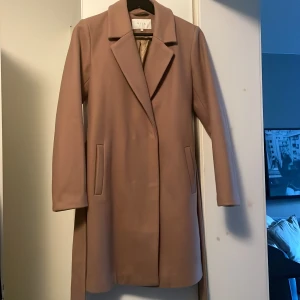 Kappa  - Höst- och vårkappa i strl 36. Färg: Camel. Knappar och midjeband. Passform: figurnära