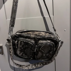 Nuuno inspirerad väska - Väska i ormskinn med flera olika fack. Ett justerbart band och ett kortare axelband. Säljes pga flytt och är i mycket bra skick 